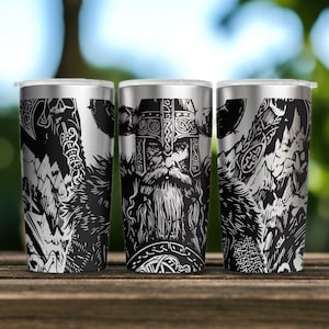 May include: A stainless steel tumbler featuring a high-contrast black and white graphic illustration of a bearded warrior wearing a horned helmet, surrounded by intricate knotwork patterns, mountain peaks, and a battle axe design.