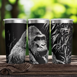 May include: A black stainless steel tumbler featuring a detailed white line art illustration of a gorilla face and surrounding jungle foliage. The cylindrical container has a metallic rim and a clear lid, showcasing a high-contrast graphic design.