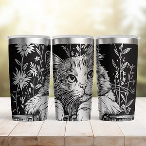 May include: A black and silver stainless steel tumbler featuring a detailed graphic illustration of a cat peering over a fence surrounded by tall wildflowers. The design is rendered in a high-contrast black and white style with a metallic finish.