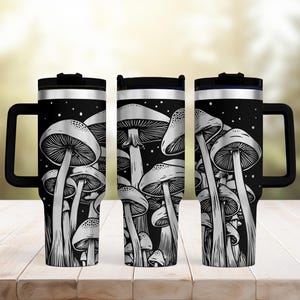 May include: Three black travel mugs with a white mushroom illustration. Each mug has a black handle and lid. The mushroom design is detailed with white lines against a black background. The mugs are displayed on a wooden surface.
