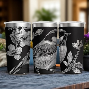 May include: A black stainless steel tumbler featuring a white line art illustration of a bird perched on a branch surrounded by floral blossoms. The cylindrical container has a metallic silver rim and a clear lid, showcasing a detailed sketch design.