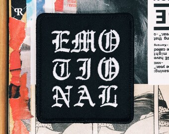 May include: Black square patch with the word "EMOTIONAL" in white gothic lettering. The patch is likely made of fabric and is set against a background of torn paper and magazine clippings.