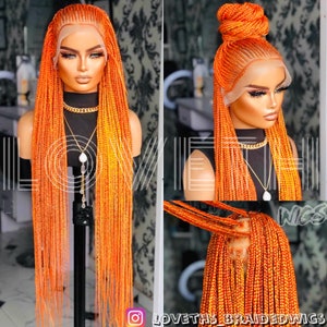 May include: A vibrant orange braided wig displayed on a mannequin head. The wig features long, individual braids with a lace front. The image also shows the wig styled in a bun. The Instagram handle @LOVETHSBRAIDEDWIGS is visible.