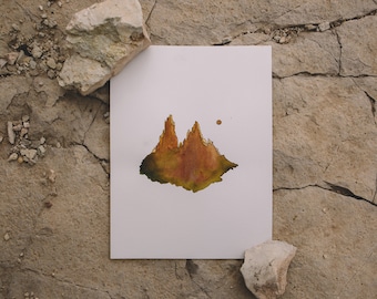 May include: A watercolor painting on white paper depicts a mountain range in shades of brown, orange, and green. The artwork is set against a textured, light brown stone surface, with two white rocks placed near the paper.