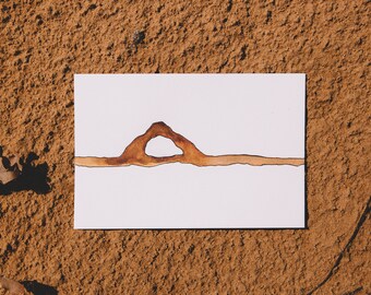 May include: A brown ink drawing of an archway on a white background. The archway is drawn with a thick line and has a rounded top. The drawing is on a piece of paper that is lying on a brown surface.