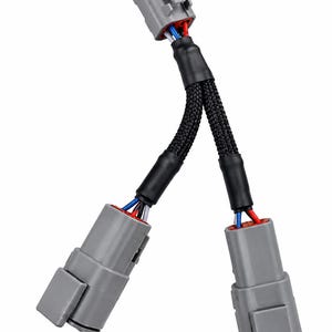 Peut inclure: Un adaptateur de faisceau de câblage électrique en forme de Y doté de trois connecteurs en plastique gris. Les fils sont enfermés dans une gaine de protection tressée noire, avec des fils isolés rouges, bleus et blancs visibles aux points de connexion.