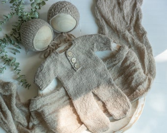 May include: A brown knitted baby outfit with a matching hat and a brown knitted wrap. The outfit has two buttons on the front.