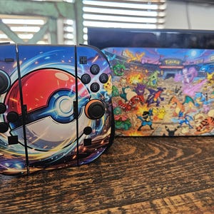 May include: A Nintendo Switch console and controllers with a colorful Pokemon theme. The controllers feature a large red and white Pokeball design. The console dock displays a vibrant scene of various Pokemon characters in a stadium setting.