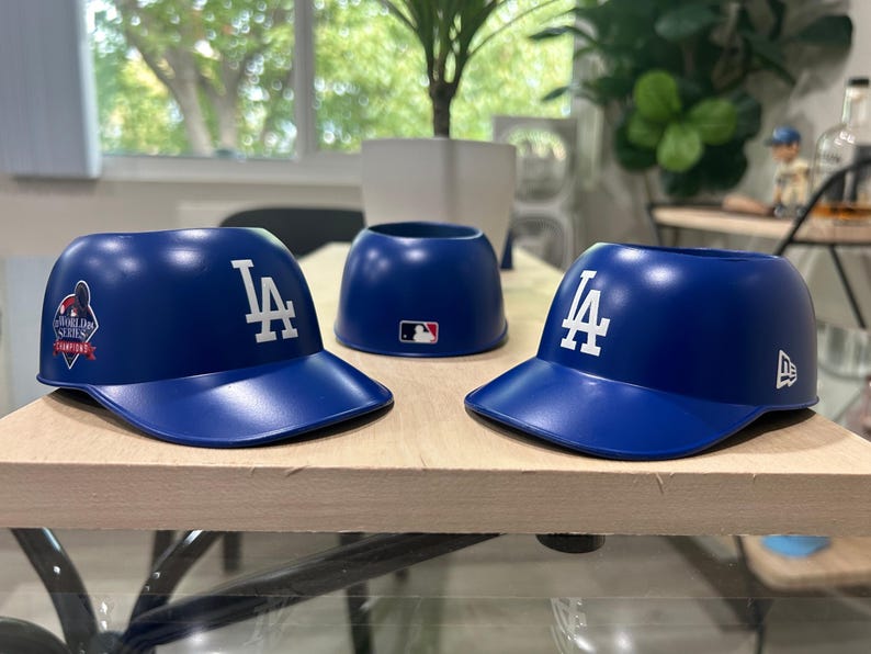 May include: Three blue plastic baseball caps with the LA logo. One cap has a World Series Champions patch. The caps are for holding drinks.