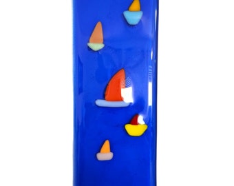 May include: A rectangular blue glass panel with a hanging hook at the top. The panel features five colorful glass sailboats in various sizes and colors, including red, orange, yellow, and blue.
