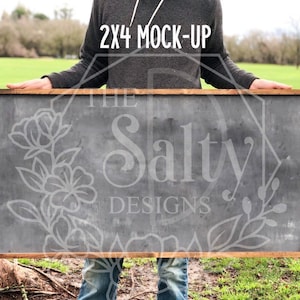 Puede incluir: Una persona sosteniendo un letrero de madera de 2x4 con una superficie de pizarra gris oscuro. El letrero tiene un marco de madera marrón y está en blanco, listo para ser personalizado. El texto "The Salty Designs" es visible débilmente en la pizarra.