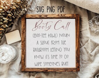 May include: A white sign with a brown wooden frame, with the text "Booty Call (BOO-TEE KAWL) NOUN A SHOUT FROM THE BATHROOM LETTING YOU KNOW IT'S TIME TO GO WIPE SOMEONE'S BUTT" in black text.