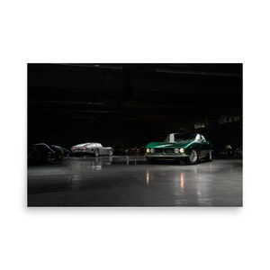 May include: Two vintage sports cars parked in a dark garage. The car in the foreground is green and the car in the background is silver.