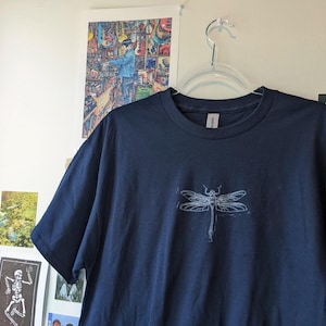 May include: A navy blue t-shirt with a white dragonfly graphic printed on the front.