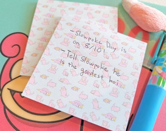 以下が含まれることがあります： 青いピンクの付箋に、「Slowpoke Day is on 8/10! Tell Slowpoke he is the goodest boi」という黒いインクで書かれたテキストがあります。
