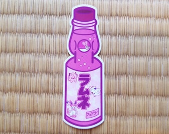 Op de afbeelding: Een roze en witte Ramune-sodafles sticker met een cartoonillustratie van Eevee en zijn evoluties. De fles heeft een roze dop en een wit etiket met het Japanse woord "Ramune" en het woord "Aardbei" in het Japans.