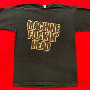 Może przedstawiać: Czarny T-shirt z nadrukiem "MACHINE FUCKIN' HEAD" w kolorze żółtym i pomarańczowym.