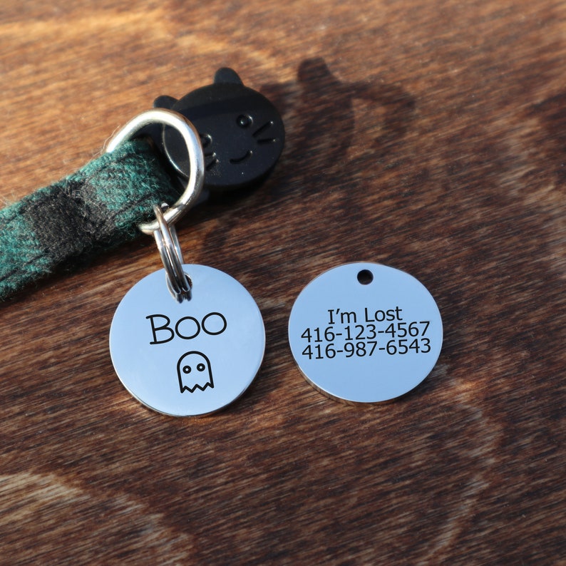 May include: Two silver dog tags with black text. One tag says "Boo" with a ghost graphic. The other tag says "I'm Lost" with two phone numbers: 416-123-4567 and 416-987-6543.