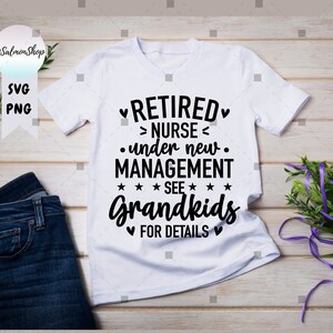 Pu&ograve; includere: Maglietta bianca con la scritta nera "RETIRED NURSE under new MANAGEMENT SEE Grandkids FOR DETAILS". Il design include cuori e stelle. La maglietta ha girocollo e maniche corte. La maglietta &egrave; su una superficie di legno chiaro.