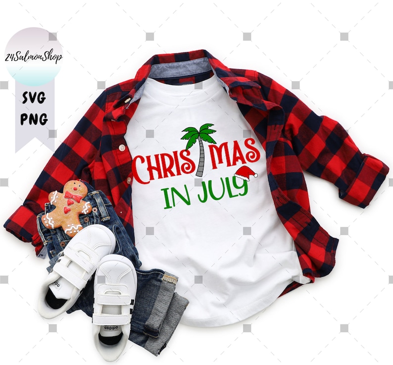 May include: A white t-shirt with red and green text that says "Christmas in July" with a palm tree and Santa hat graphic. The shirt is folded and displayed on a red and black plaid shirt and blue jeans.