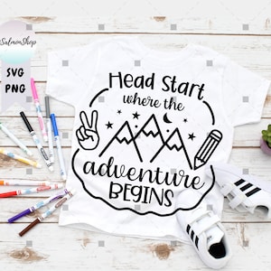May include: White t-shirt with a black and white graphic design of mountains, a pencil, a peace sign, and the text "Head Start where the adventure begins".