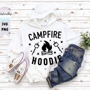 Könnte beinhalten: Weißer Hoodie mit schwarzem Text, der "Campfire Hoodie" sagt, mit einem Grafikmotiv von einem Lagerfeuer, Sternen und Marshmallows.