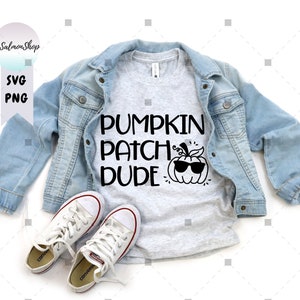 May include: A gray t-shirt with the text "Pumpkin Patch Dude" and a cartoon pumpkin wearing sunglasses. The shirt is on a white background with a denim jacket and white sneakers.