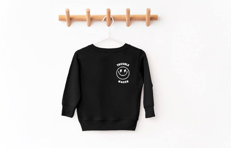 May include: Black long-sleeve sweatshirt with a white graphic of a smiley face with lightning bolts and the text "Trouble Maker".
