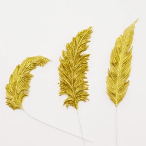 May include: Three gold-colored feathers with white stems on a white background.
