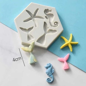 Peut inclure: Un moule en silicone blanc avec quatre formes de queue de sirène et d'étoile de mer. Il y a quatre queues de sirène finies et une étoile de mer de différentes couleurs, dont le jaune, le bleu, le rose et le vert. Le moule mesure 4 cm de long.