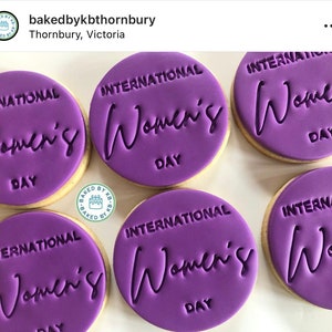 May include: Six purple decorated cookies, each with the text "International Women's Day".