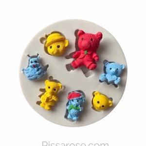 May include: Silicone mold with seven bear-shaped cavities. The mold is white and features bears in various colors, including red, blue, yellow, and green. The bears are wearing hats and clothes.