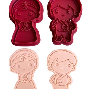 May include: Two sets of cookie cutters, one red and one pink, shaped like a boy and girl wearing traditional Korean clothing.