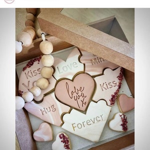 May include: A heart-shaped box filled with cookies decorated with different messages, including "Love you", "Kiss", "Hug", "Forever", and "Mine". The cookies are arranged in a puzzle-like pattern and are decorated with a marbled design.