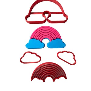 Puede incluir: Un juego de cortadores de galletas de arcoíris y nubes. El juego incluye dos cortadores de arcoíris, uno con rayas rosas y azules y el otro con rayas rojas, y tres cortadores de nubes.