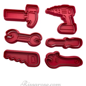 May include: Set of six red plastic cookie cutters shaped like tools: a hammer, a drill, a wrench, a screwdriver, a saw, and a wrench.