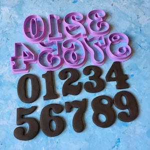 May include: A set of ten purple plastic number cookie cutters and ten black fondant numbers. The cookie cutters are in a vintage style font and the fondant numbers are in a more modern font.