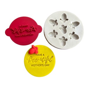 May include: A set of two red silicone stamps for baking and decorating. One stamp features the text "Have a Bee-utiful Mother's Day" with a small bee image. The other stamp features the text "Bee-utiful" with a small bee image.
