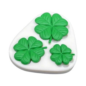 May include: A white, oval-shaped mold with three green shamrock designs. The shamrocks vary in size, with detailed leaf patterns. The image is well-lit, highlighting the vibrant green color of the shamrocks.