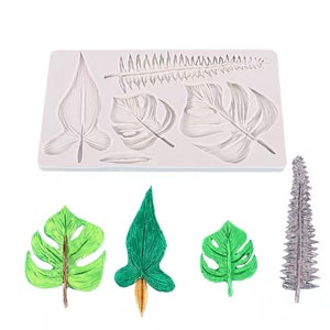 May include: Silicone mold with six different leaf shapes, including fern, monstera, and palm leaves. The mold is shown with finished leaf shapes made from fondant or gum paste.