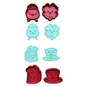 May include: A collection of St. Patrick's Day-themed cookie cutters in red and teal. The set includes a pot of gold, a four-leaf clover, a beer mug, and a leprechaun hat, all with smiling faces.