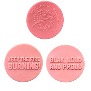 May include: Three pink round rubber stamps with raised lettering. The first stamp says "Celebrating NAIDOC Week" and features a stylized Aboriginal flag design. The second stamp says "Keep the fire burning!" and the third stamp says "Blak, Loud and Proud."