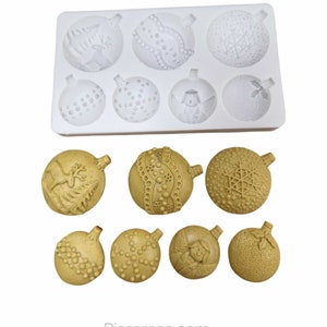 May include: A white silicone mold with six round cavities shaped like Christmas ornaments. The mold is filled with six golden brown Christmas ornaments with various designs, including a reindeer, snowflakes, and a Christmas angel.