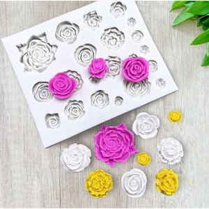 May include: A white silicone mold with various rose shapes and several detached rose-shaped decorations in pink, white, and yellow. The mold has different sized rose impressions. The detached roses are in various sizes.