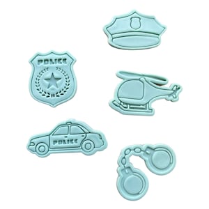 Op de afbeelding: Set van vijf blauwe plastic koekjesvormen in de vorm van een politiepet, een politiebadge, een politieauto, een helikopter en handboeien. De vormen zijn bedoeld voor het maken van koekjes of andere gebak.