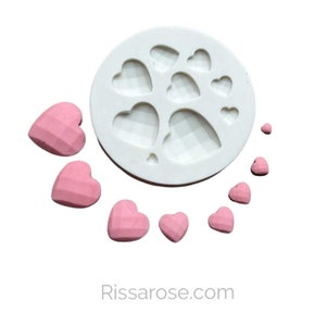 May include: A white silicone mold with eight heart-shaped cavities. The mold is surrounded by pink heart-shaped candies.