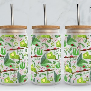 Puede incluir: Tres vasos de vidrio transparentes con tapas de madera y diseños de camaleones y mariquitas verdes y rojos. Cada vaso tiene una pajita de acero inoxidable.