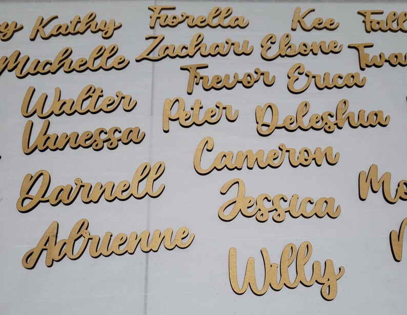 May include: A collection of individual wooden name cutouts in a cursive script font. The names include Kathy, Fiorella, Kee, Michelle, Zacharu, Ebone, Walter, Frevor, Erica, Vanessa, Peter, Deleshia, Cameron, Darnell, Jessica, Adrienne, and Willy.
