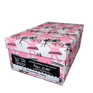 Pu&ograve; includere: Scatola rettangolare con motivo floreale rosa e bianco. La scatola presenta il testo "hi! I'm Ginny" e "Vogue Dolls". &Egrave; etichettata come bambola da collezione da 20 cm.