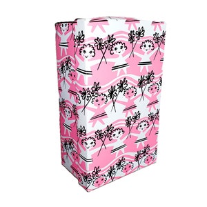 Pu&ograve; includere: Una scatola regalo rettangolare alta con un motivo ripetuto di figure sorridenti che tengono fiori su uno sfondo rosa e bianco. La scatola &egrave; bianca con un motivo a strisce rosa ondulate.